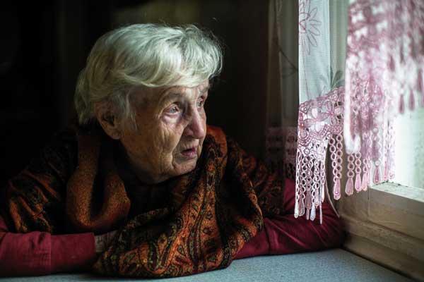 Äldre kvinna som tittar ut genom ett fönster